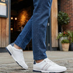 Lifestyle shot of white Bugatti sneakers with striped detail worn with blue jeans.