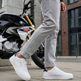 Lifestyle close-up of white bugatti Helium Comfort Sneakers, worn with grey pants and standing next to a motorcycle.
