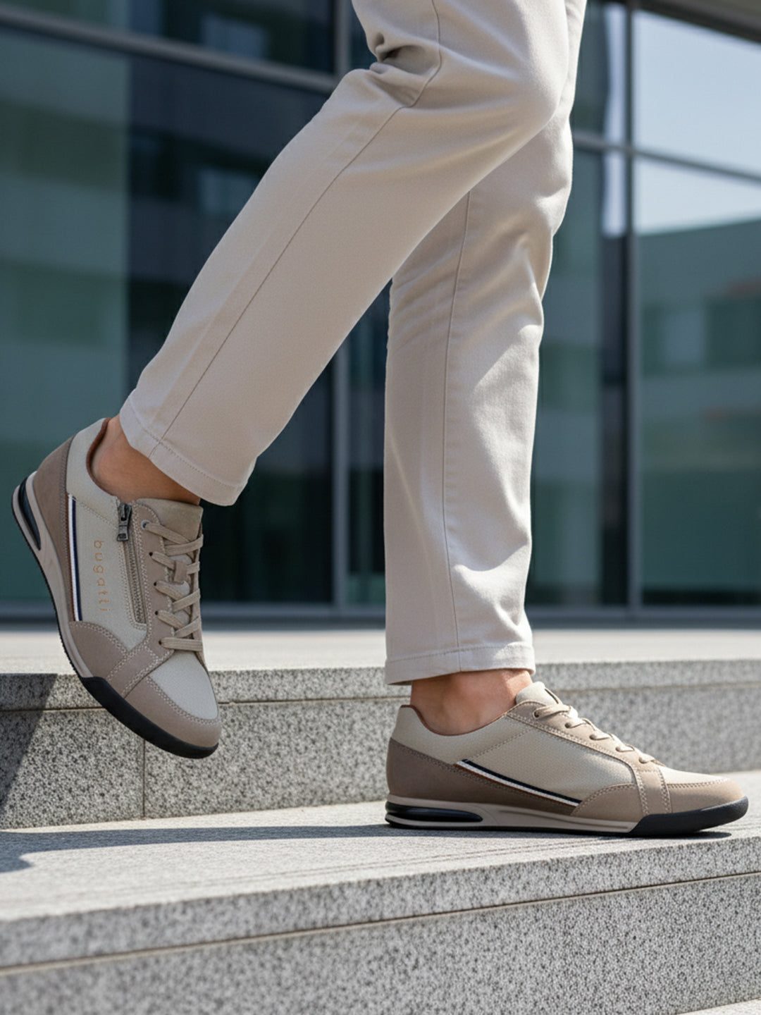 Lifestyle shot of bugatti Trevor beige comfort sneakers, with a zipper, worn with beige pants on steps.
