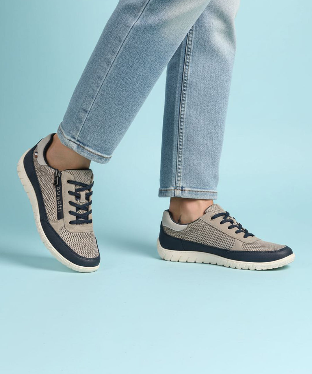 Lifestyle shot of bugatti Bermudas taupe comfort sneakers, with blue trim and dark blue laces, worn with jeans.