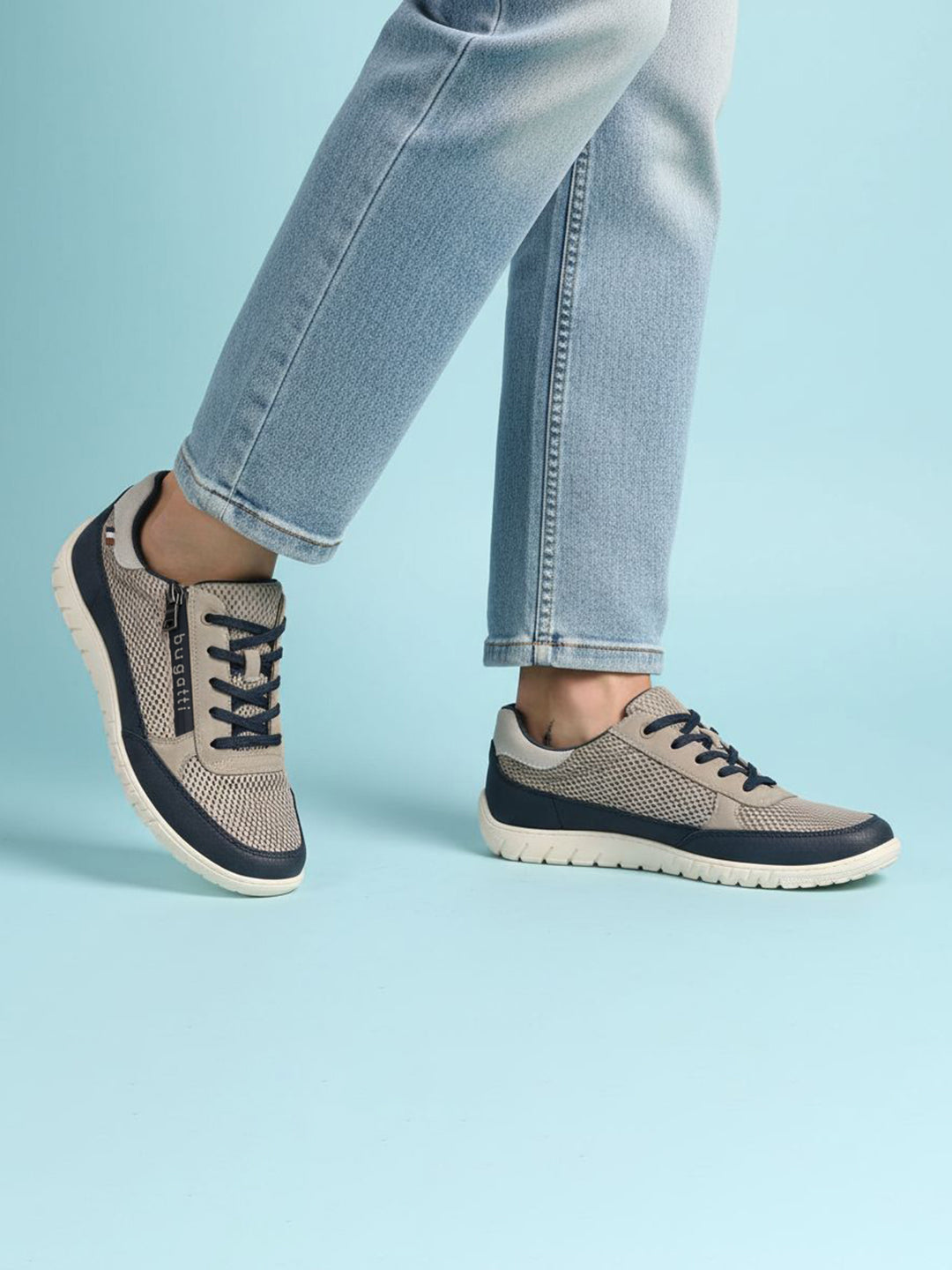 Lifestyle shot of bugatti Bermudas taupe comfort sneakers, with blue trim and dark blue laces, worn with jeans.