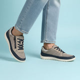 Lifestyle shot of bugatti Bermudas taupe comfort sneakers, with blue trim and dark blue laces, worn with jeans.