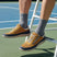 Lifestyle shot of bugatti Bermudas yellow comfort sneakers worn with gray socks on a tennis court.
