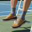 Lifestyle shot of bugatti Bermudas yellow comfort sneakers worn with gray socks on a tennis court.

