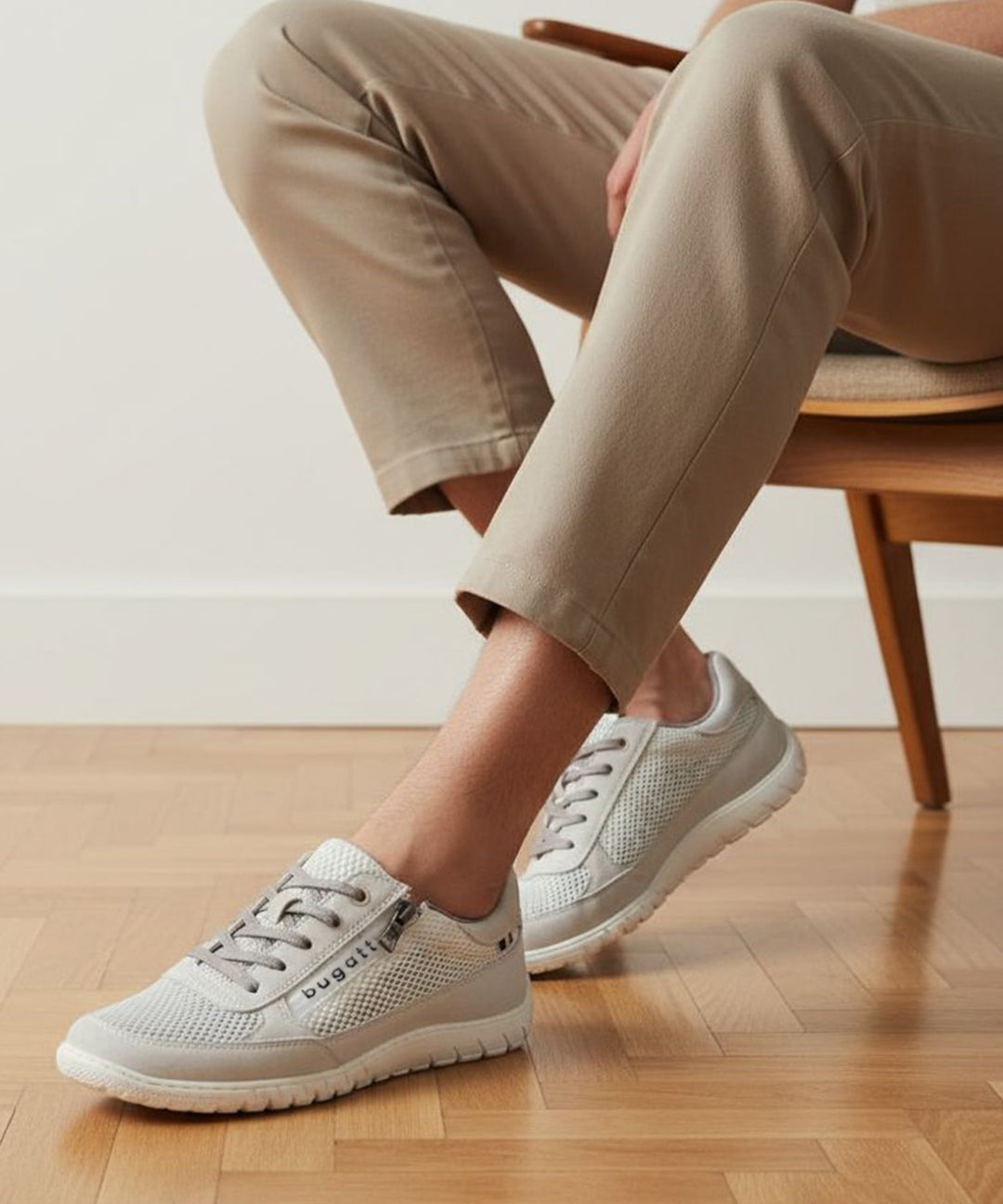Lifestyle image of bugatti white sneakers, shown with a mesh texture, zipper accent, and worn with casual trousers.