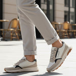 Lifestyle shot of bugatti Jerit Beige Comfort Sneakers, with zipper detail, worn with cuffed grey pants on a paved surface.
