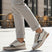 Lifestyle shot of bugatti Jerit Beige Comfort Sneakers, with zipper detail, worn with cuffed grey pants on a paved surface.
