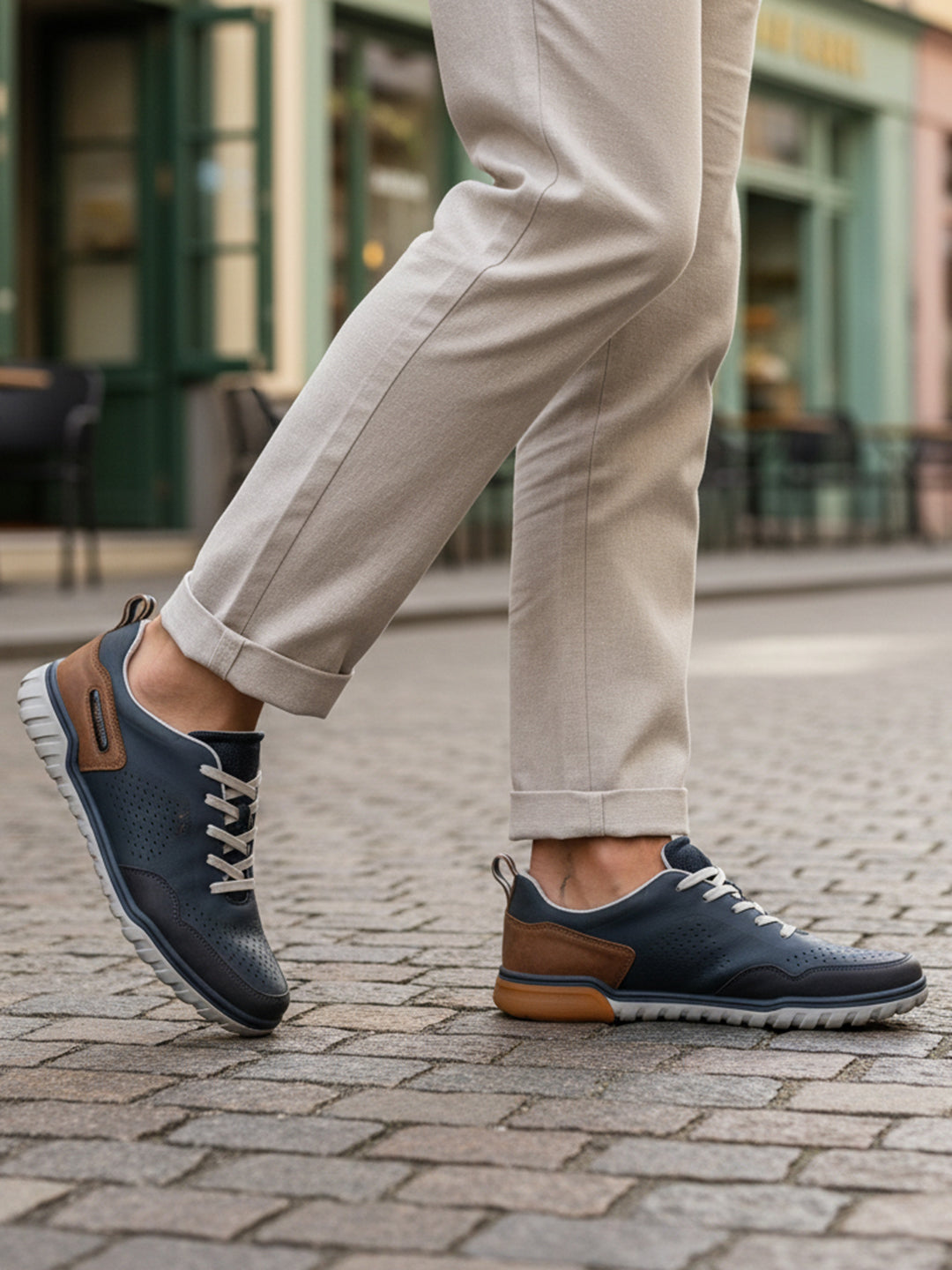 Lifestyle shot of bugatti Samana dark blue sneakers, with brown accents and a perforated upper, paired with tan trousers.
