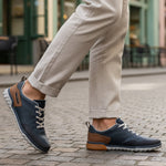 Lifestyle shot of bugatti Samana dark blue sneakers, with brown accents and a perforated upper, paired with tan trousers.
