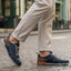 Lifestyle shot of bugatti Samana dark blue sneakers, with brown accents and a perforated upper, paired with tan trousers.
