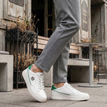 Lifestyle shot of white bugatti Humus Premium Leather Comfort Mid Top Sneakers with green accents, worn with gray pants.