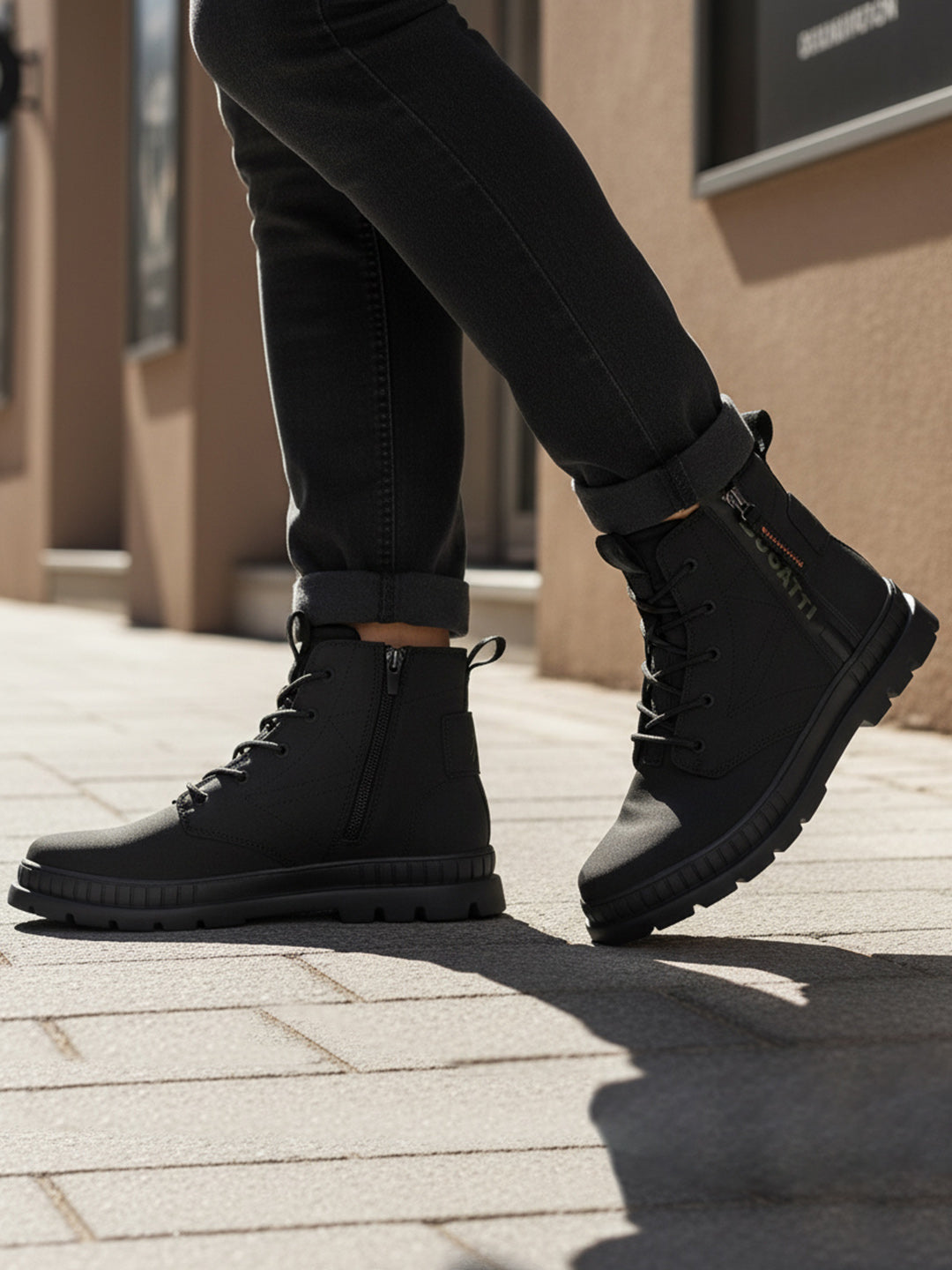 Lifestyle shot of bugatti Pallario comfort black casual boots, with zipper detail and lug sole, worn with dark rolled jeans.

