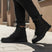 Lifestyle shot of bugatti Pallario comfort black casual boots, with zipper detail and lug sole, worn with dark rolled jeans.
