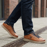 Lifestyle close-up of bugatti Fiero cognac leather sneakers with dark denim jeans on a city street.