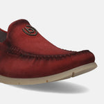 Red leather slip-on shoe by bugatti, featuring decorative stitching and a branded metal emblem.