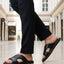 bugatti Cobie black leather sandals with a cross-strap design, paired with black trousers in a lifestyle shot.
