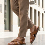 Lifestyle view of bugatti cognac leather sandals with adjustable back strap worn with tan pants.
