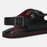Cropped view of a black bugatti sandal in leather with buckle straps and a red accent stripe.
