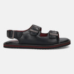 Side view of a black leather bugatti sandal with two buckled straps and red stripe detail.
