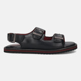 Side view of a black leather bugatti sandal with two buckled straps and red stripe detail.
