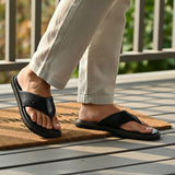 Lifestyle view of bugatti Cobie comfort thong sandals in black leather, paired with linen trousers.