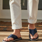 Lifestyle shot of bugatti Cobie comfort thong sandals in dark blue, worn with white casual pants.
