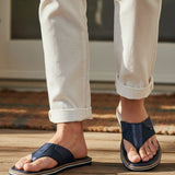 Lifestyle shot of bugatti Cobie comfort thong sandals in dark blue, worn with white casual pants.
