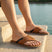 Lifestyle image of bugatti Cobie cognac leather thong sandals, with dark accent stripe and white soles.