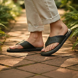 Lifestyle shot of bugatti Cobie dark green leather thong sandals, worn with rolled khaki pants, on a brick path.
