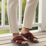 Lifestyle image of bugatti Cobie red premium leather sandals with crossing straps, worn with beige pants on a wooden deck.
