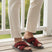 Lifestyle image of bugatti Cobie red premium leather sandals with crossing straps, worn with beige pants on a wooden deck.
