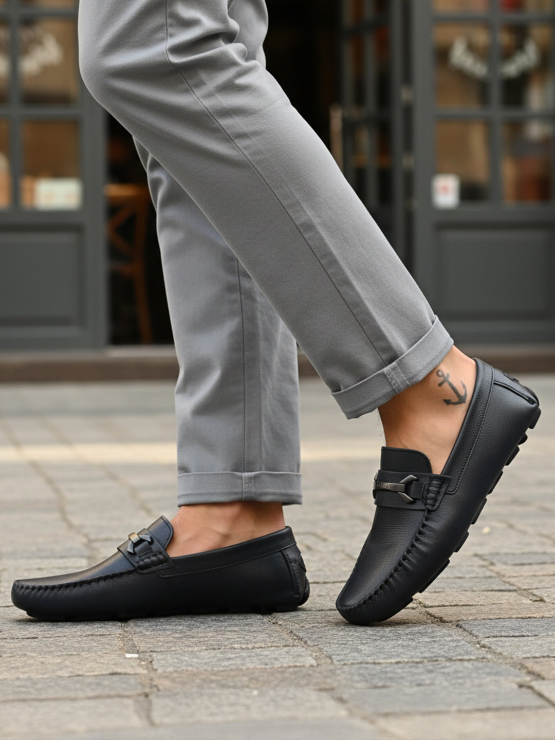 Lifestyle shot of bugatti Olexa dark blue leather slip-ons with a metal accent, worn with gray pants.