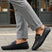 Lifestyle shot of bugatti Olexa dark blue leather slip-ons with a metal accent, worn with gray pants.