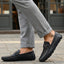 Lifestyle shot of bugatti Olexa dark blue leather slip-ons with a metal accent, worn with gray pants.