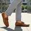 Lifestyle image of bugatti Olexa cognac leather slip-on shoes with rolled grey trousers.
