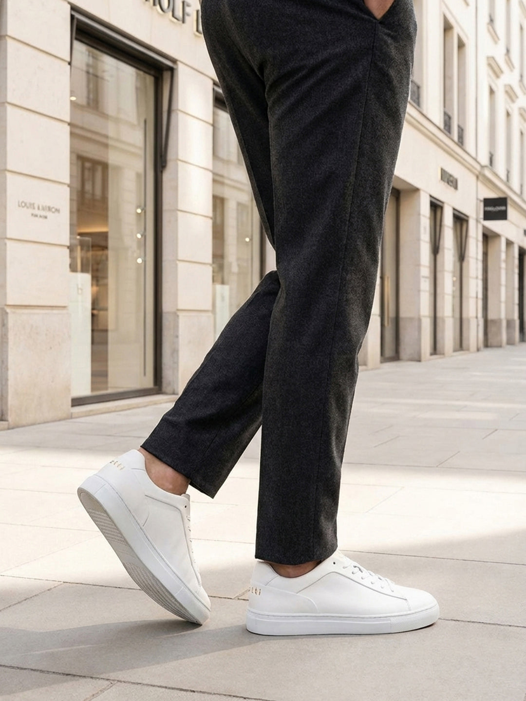 Lifestyle shot of bugatti Fogg white premium leather sneakers, paired with grey trousers and white pavement.
