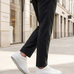 Lifestyle shot of bugatti Fogg white premium leather sneakers, paired with grey trousers and white pavement.
