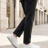 Lifestyle shot of bugatti Fogg white premium leather sneakers, paired with grey trousers and white pavement.
