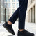 Lifestyle cropped shot of bugatti Fogg Black leather sneakers paired with dark trousers on tiled pavement.
