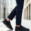 Lifestyle cropped shot of bugatti Fogg Black leather sneakers paired with dark trousers on tiled pavement.