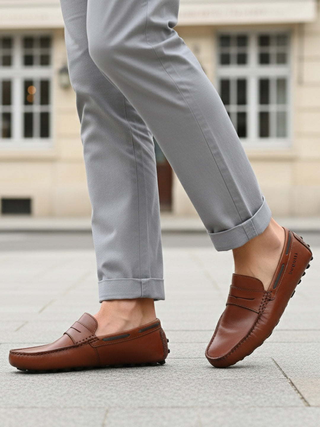 Lifestyle view of bugatti Manfield cognac leather slip-on shoes with penny loafer detailing and gray pants.