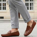 Lifestyle view of bugatti Manfield cognac leather slip-on shoes with penny loafer detailing and gray pants.