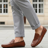 Lifestyle view of bugatti Manfield cognac leather slip-on shoes with penny loafer detailing and gray pants.