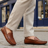 Lifestyle image of bugatti Manfield cognac leather slip-on shoes with visible textured beige pants on a cobblestone street.