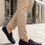 Lifestyle close-up of bugatti Manfield dark blue leather slip-on shoes worn with tan pants on a cobblestone street.
