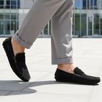 Lifestyle shot of a bugatti Manfield black leather slip-on shoe, paired with gray casual pants.
