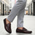 Lifestyle shot of a bugatti Linex slip-on shoe in mid-brown leather, paired with gray slacks and worn on a tiled street.
