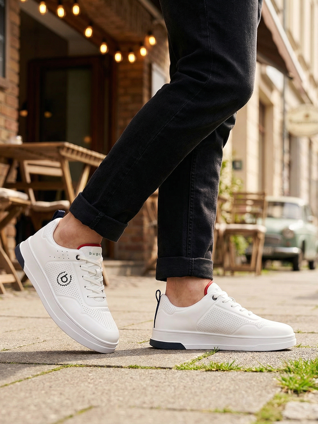Lifestyle shot of bugatti Franc white leather sneakers, with perforated details, worn with dark jeans.
