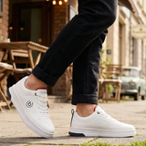 Lifestyle shot of bugatti Franc white leather sneakers, with perforated details, worn with dark jeans.
