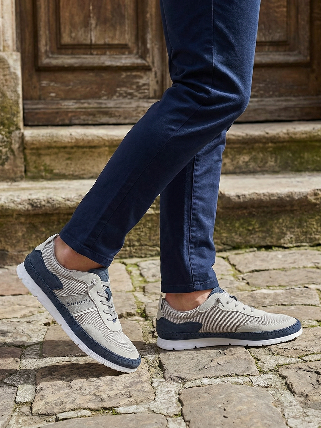Lifestyle close-up of Bugatti Clipperton sand comfort low top sneakers with dark blue chinos on a stone surface.
